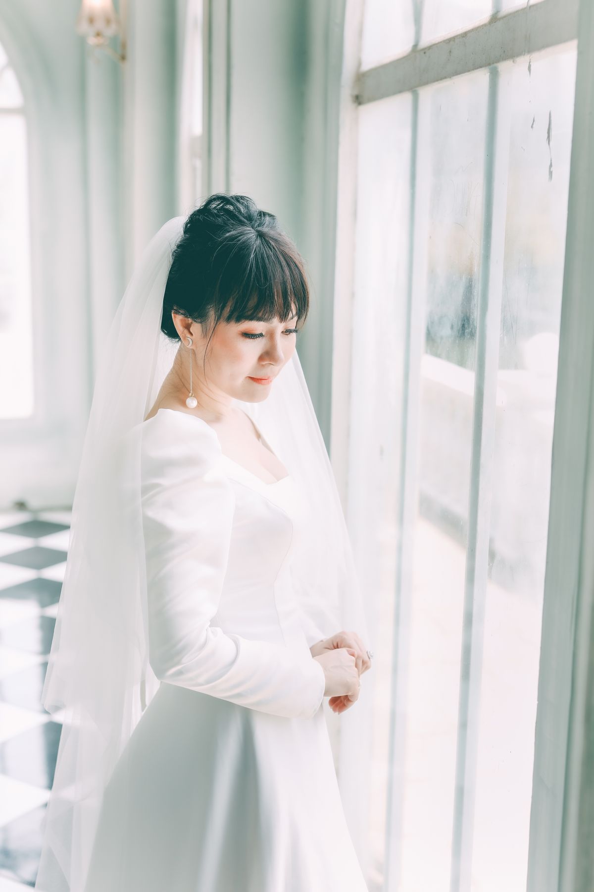 Bride in a white gown standing beside a bright window