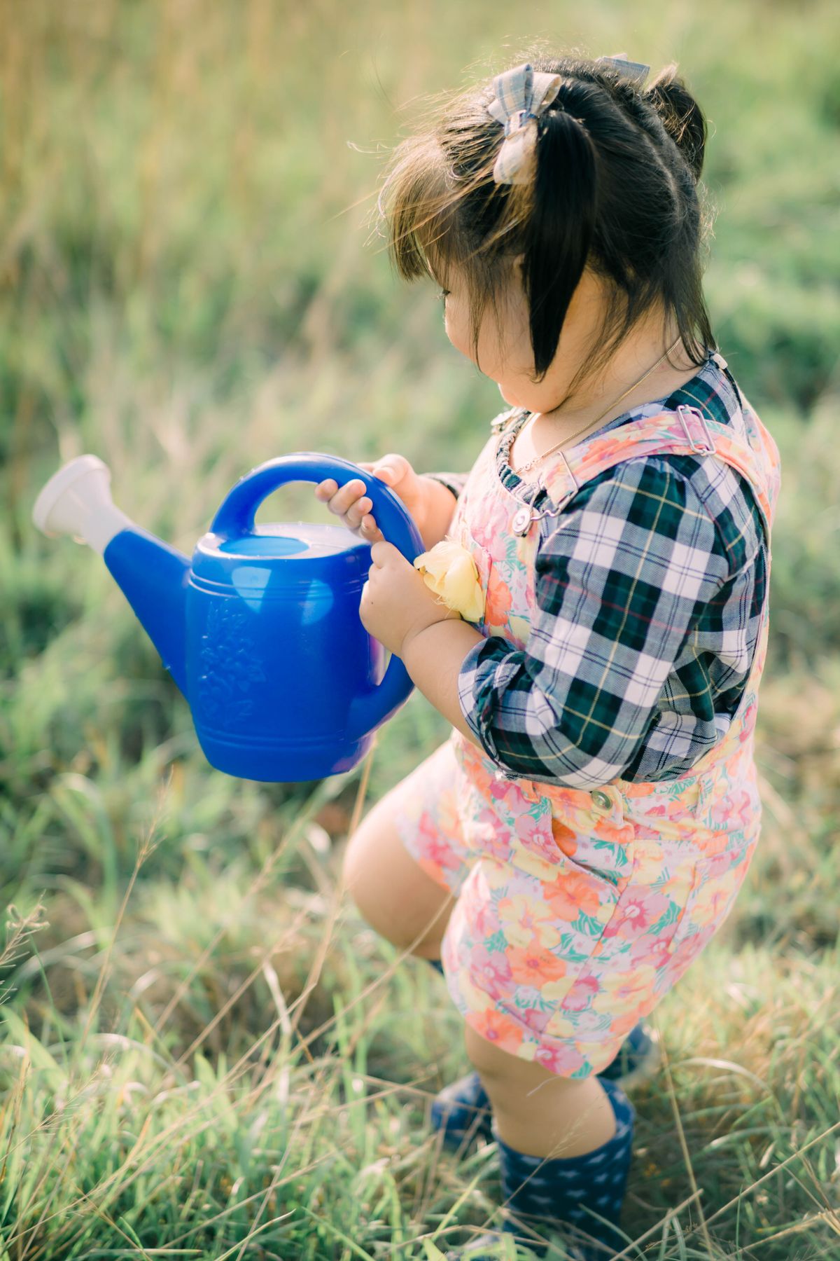 First birthday party favor ideas with a toddler holding a blue watering can in a garden for watering can favors