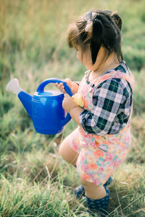 Free Adorable child with a blue watering can in a grassy garden setting, embodying playfulness and nature. Stock Photo