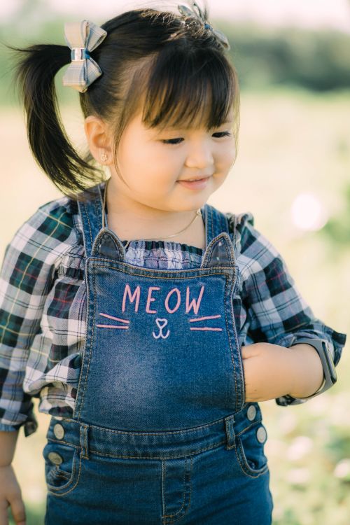 Free Adorable young girl in denim overalls playing outdoors, exuding innocence and charm. Stock Photo