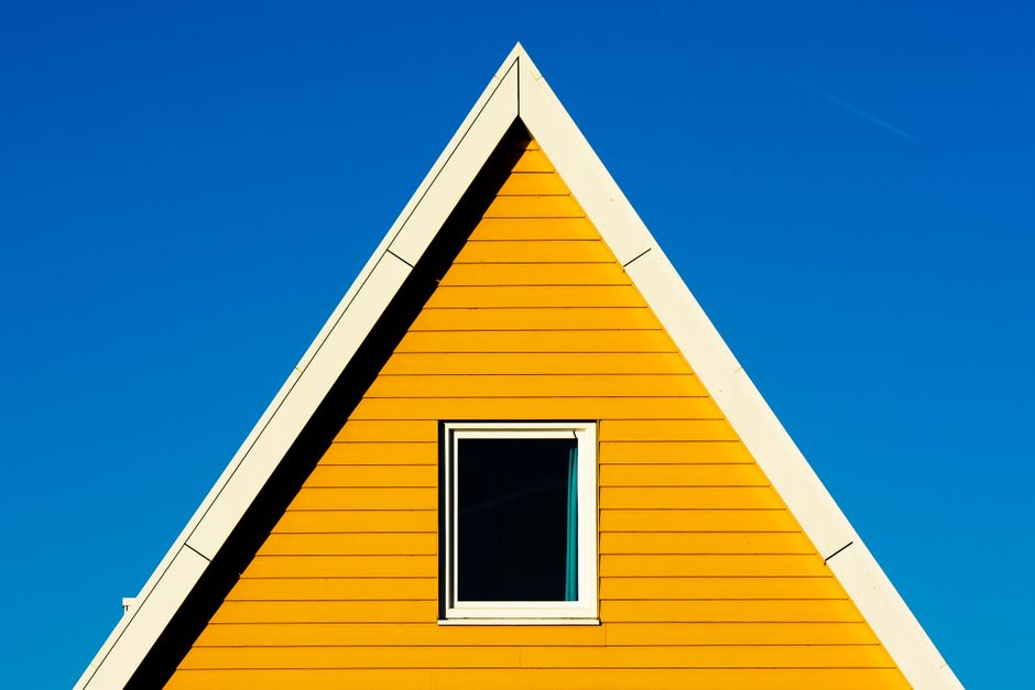 A striking yellow house with a triangle roof set against a vivid blue sky, showcasing modern architectural design.