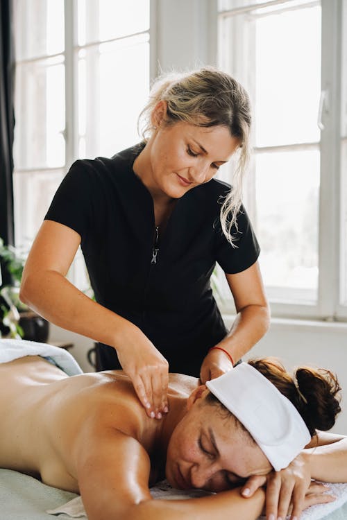 Masseuse in a Black Polo Shirt Massaging a Woman's Back