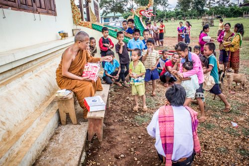 Free A Buddhist monk distributing items to a group of children and adults at a temple in a rural area. Stock Photo