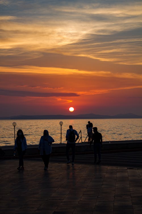 Silhouettes of People Standing Near the Sea During Sunset