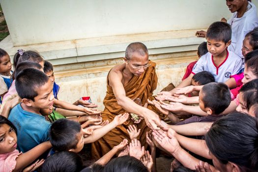 A monk shares offerings with a group of children outdoors, promoting compassion and connection. — photo by Suraphat Nuea-on
