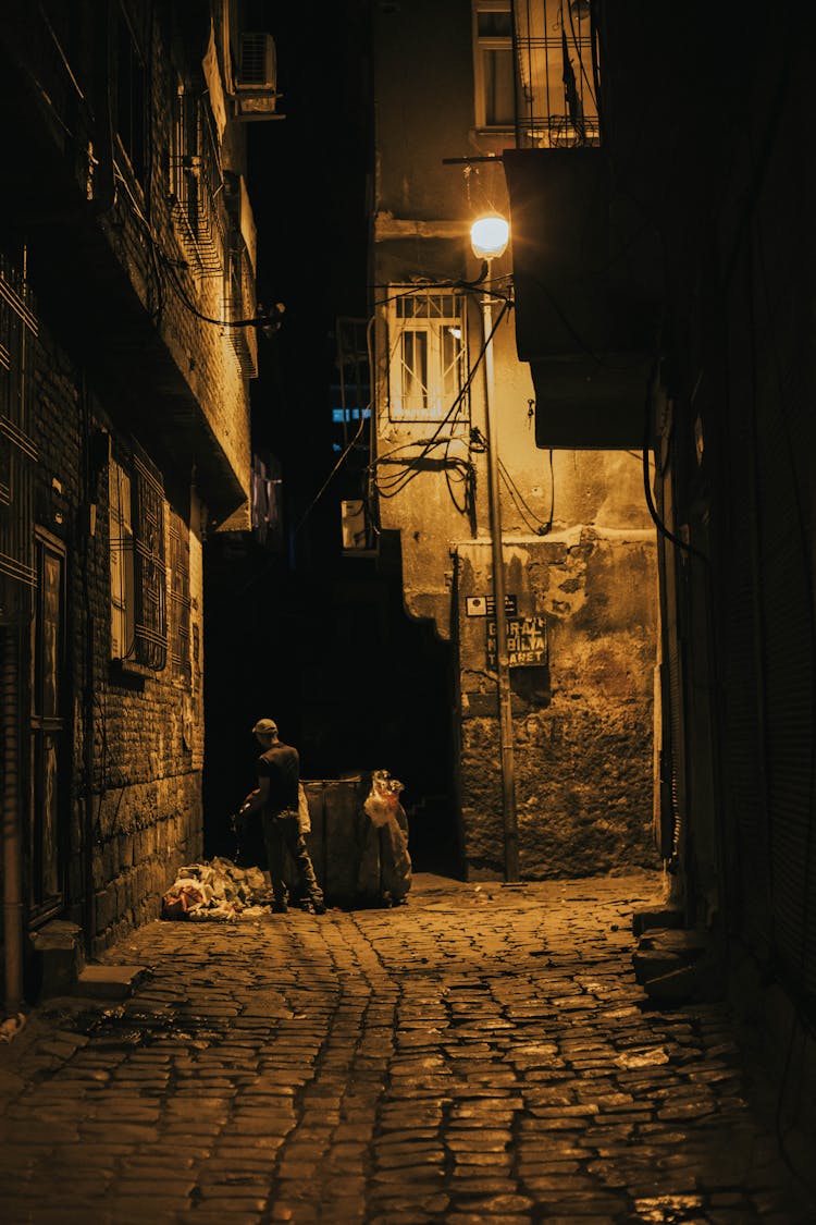 Man Standing Beside Garbage On An Alley During Night Time