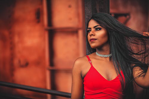 Close-Up Photo of a Woman in a Red Spaghetti Strap Top Touching Her Hair