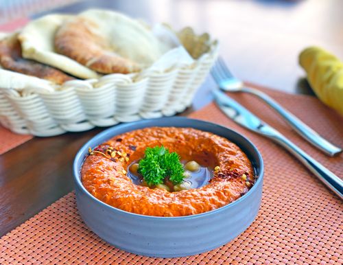 Free Close-up of spicy red hummus garnished with parsley, served with flatbread in a cozy setting. Stock Photo