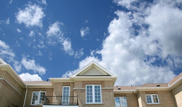 A modern brick house with large windows set against a bright blue sky with fluffy clouds.