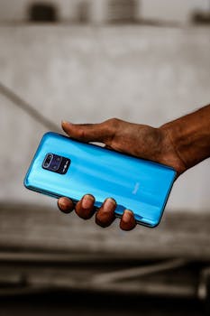 Close-up shot of a hand holding a blue smartphone outdoors, in Dhaka, Bangladesh.