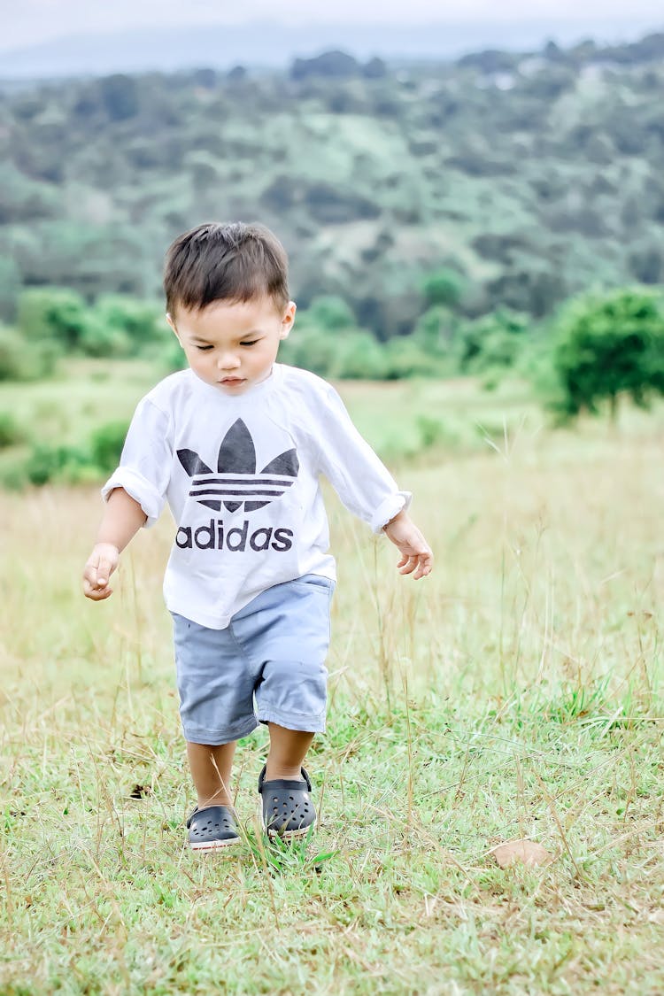 Cute Kid In A White Crew Neck Shirt Walking On The Grass