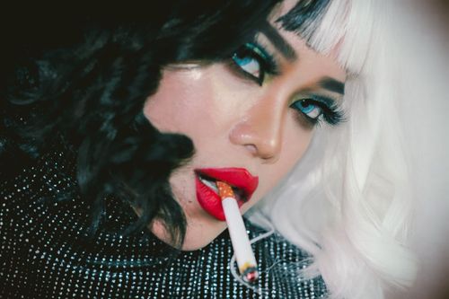 Free Artistic close-up of a woman with creative makeup, red lips, and a cigarette. Stock Photo