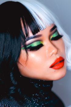 Close-up of a woman wearing vibrant makeup and two-toned hair, posing with eyes closed.