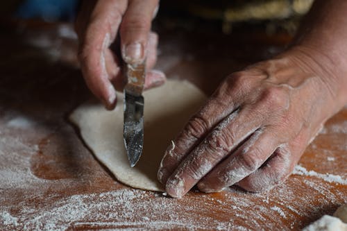 Photo of a Person's Hands Holding a Knife Near a Dough