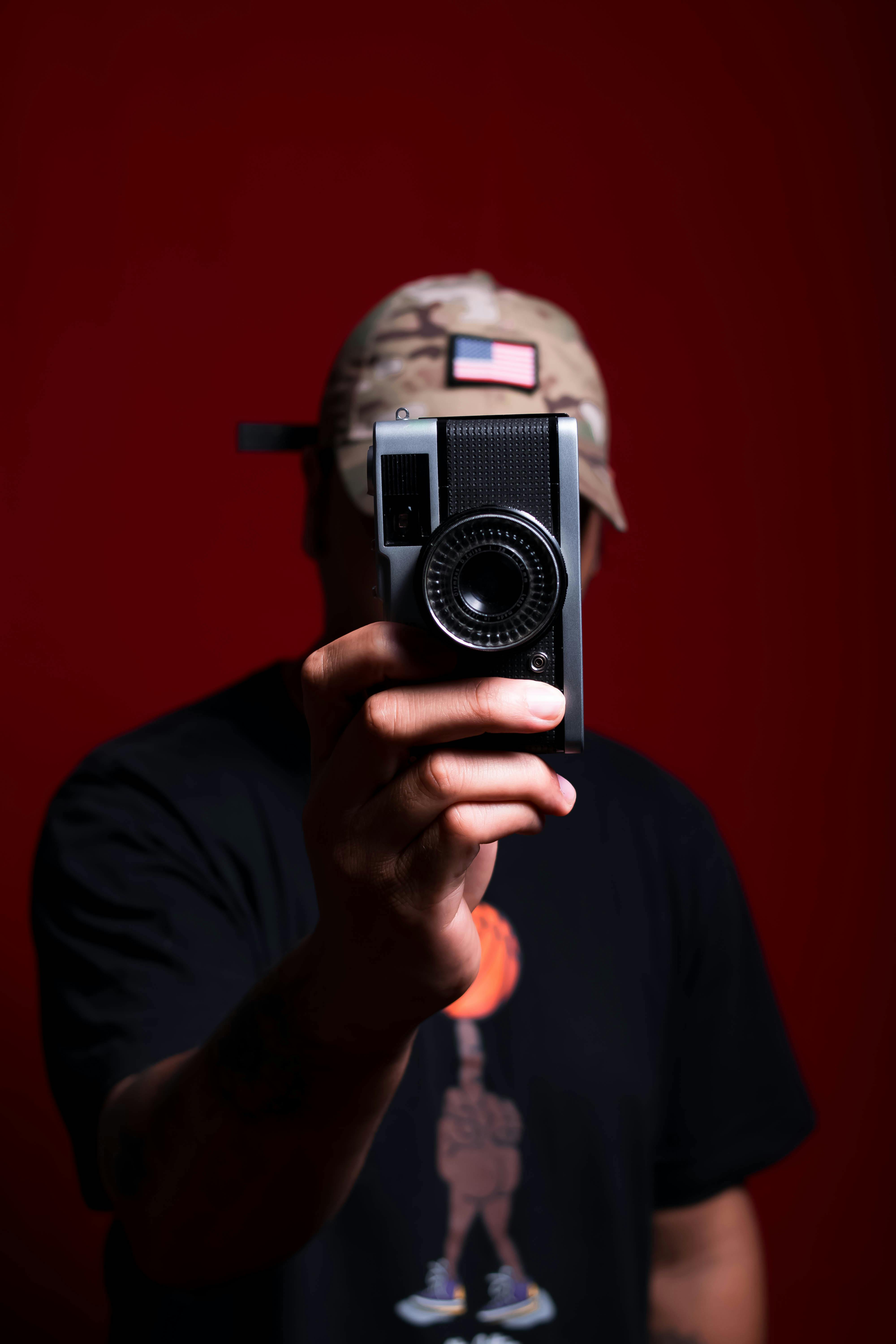 Free Close-up of a person holding a vintage camera against a bold red background, capturing creativity. Stock Photo