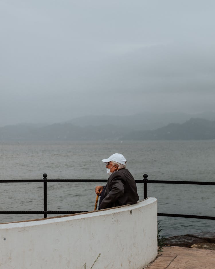 Unrecognizable Old Man Sitting On Embankment Near Water