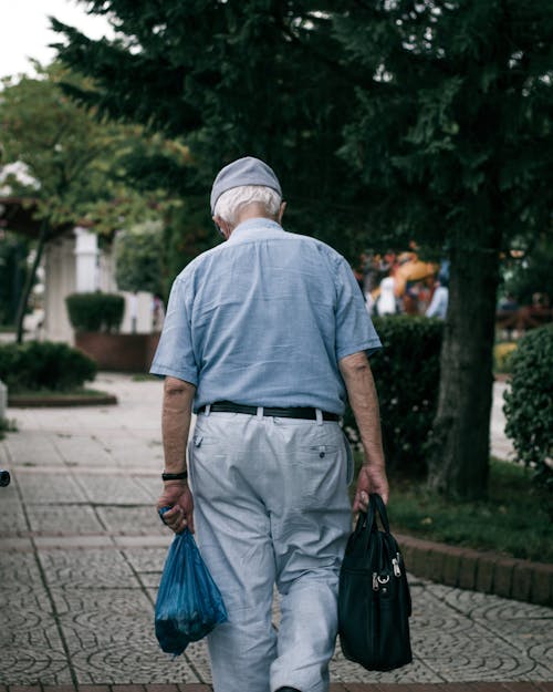 Back View of an Elderly Man Walking while Carrying Two Bags