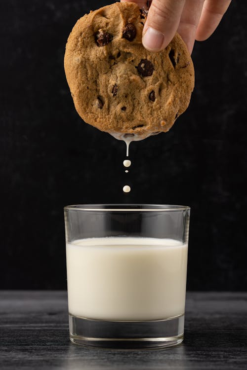 Free Photo of a Person's Hand Dipping a Cookie in a Glass of Milk Stock Photo