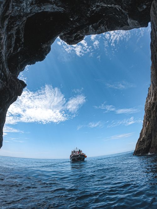 Free A boat navigates through crystal clear ocean waters towards a stunning cave opening against a bright blue sky. Stock Photo