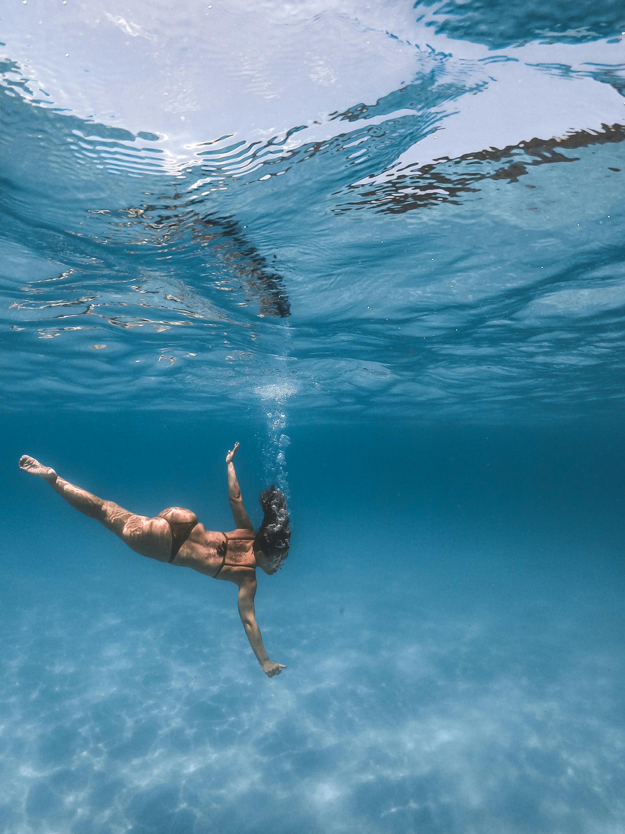 一名女子在清澈的海水中游泳，周围都是气泡和阳光