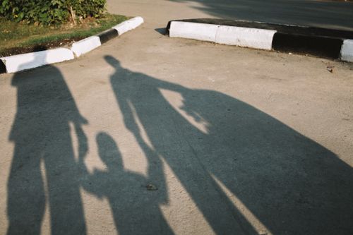 Free Silhouettes of a family holding hands cast shadows on a sunny pavement. Stock Photo