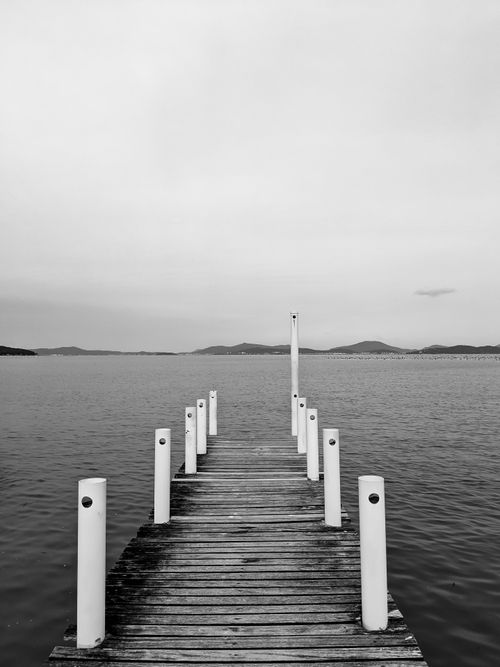 Free Timeless black and white image of a wooden dock extending into a calm lake under a cloudy sky. Stock Photo