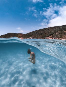 A woman gracefully diving underwater in clear blue sea under a bright sky.