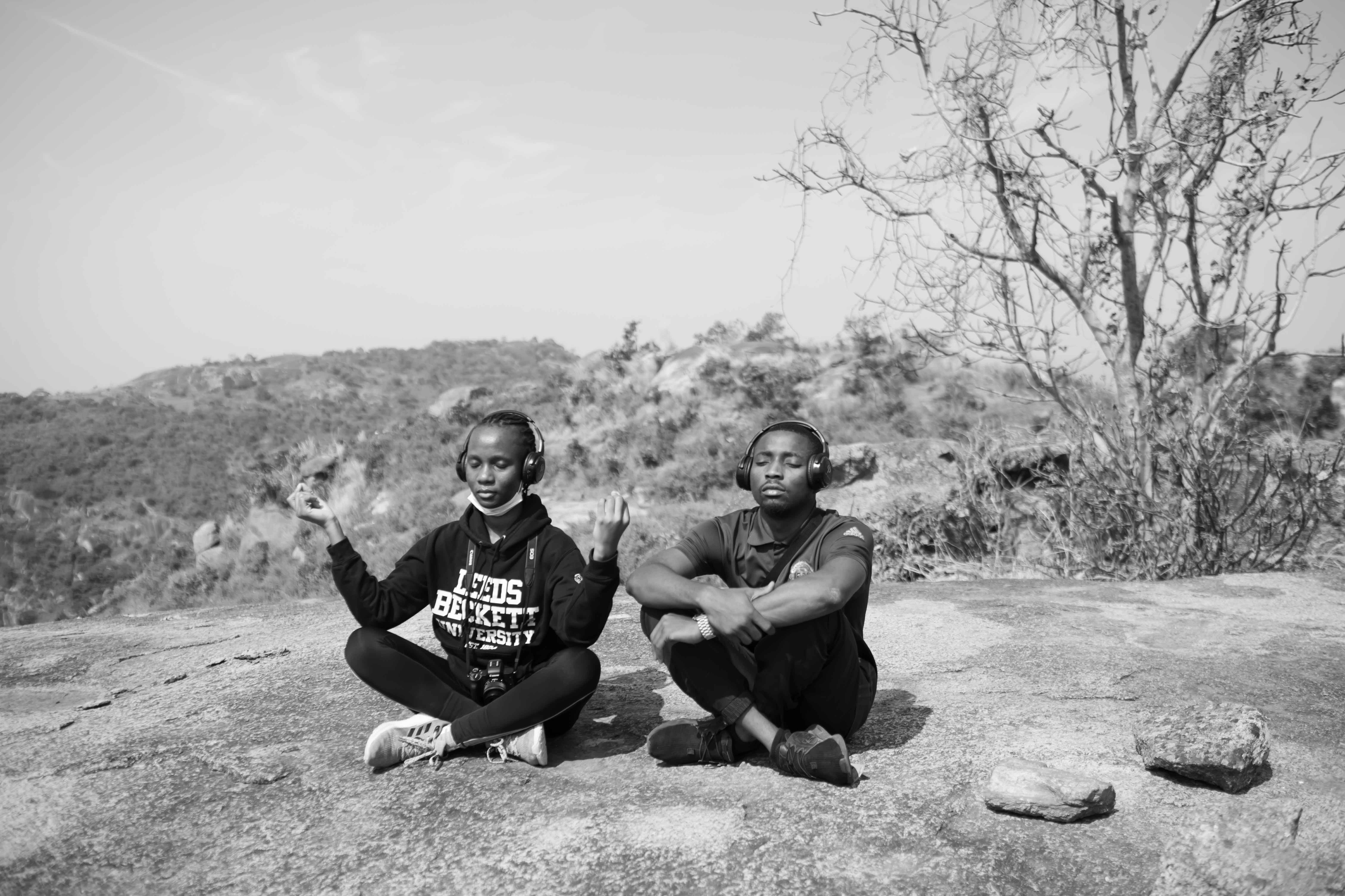 Two friends meditate outdoors listening to music with wireless headphones in a serene, natural setting.