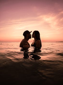 Silhouette of a romantic couple kissing in ocean waters during a stunning sunset.
