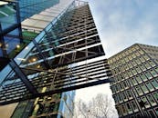 从低角度仰望现代摩天大楼，玻璃立面倒映着天空，定格了城市建筑的景象