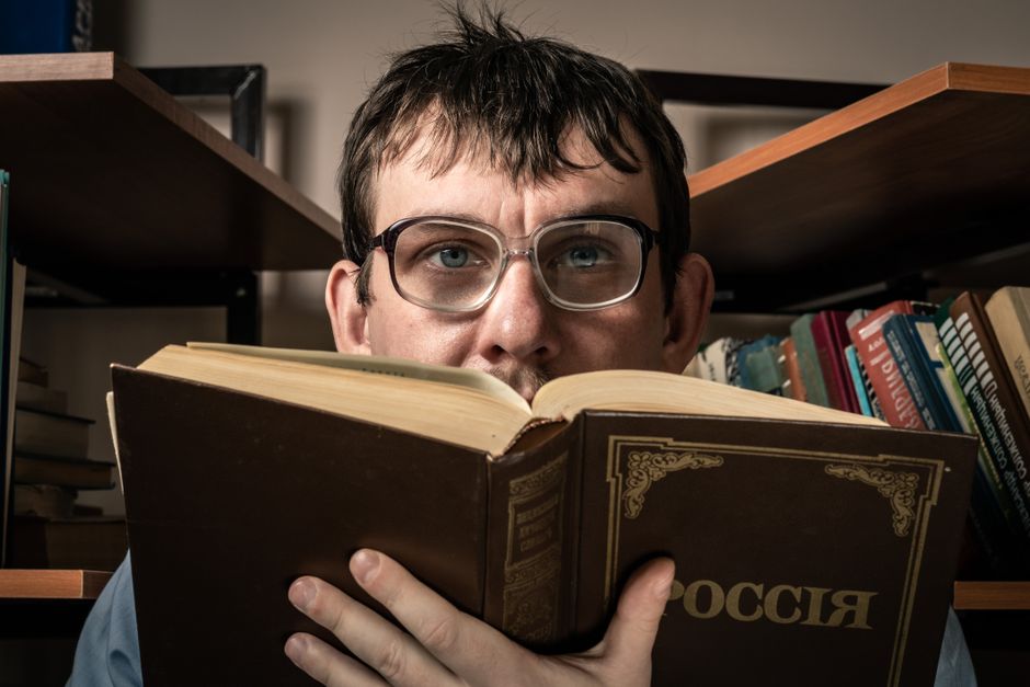 Man with glasses reading a book titled 'Россия' in a cozy library setting. Man with glasses reading a book titled 'Россия' in a cozy library setting.