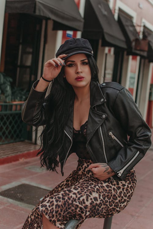 Woman in Black Leather Jacket and Leopard Print Skirt Sitting on Metal Railing