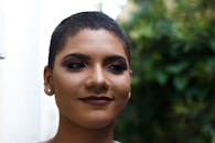 一位妆容大胆、短发自信的女性，在户外花园中露出愉快的表情