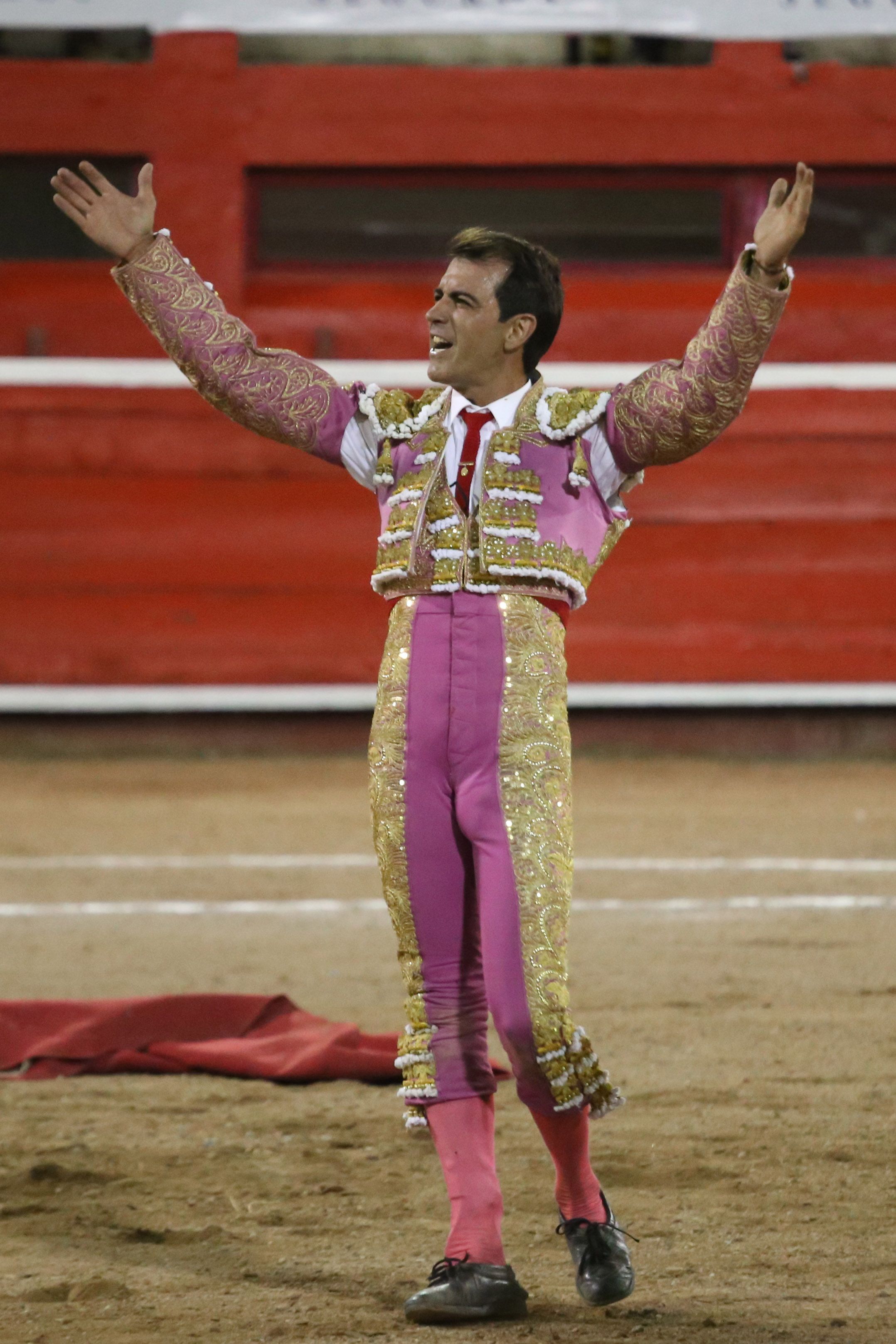 Matador in traditional suit raises arms in victory at a bullfighting ring.
