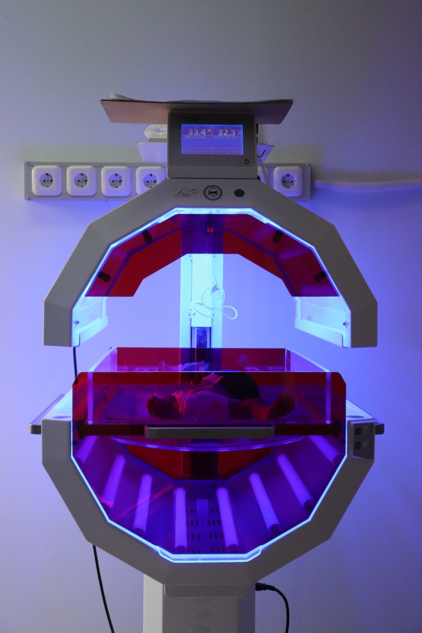 Hoogtechnologische neonatale couveuse met paarse verlichting in een ziekenhuiskamer.