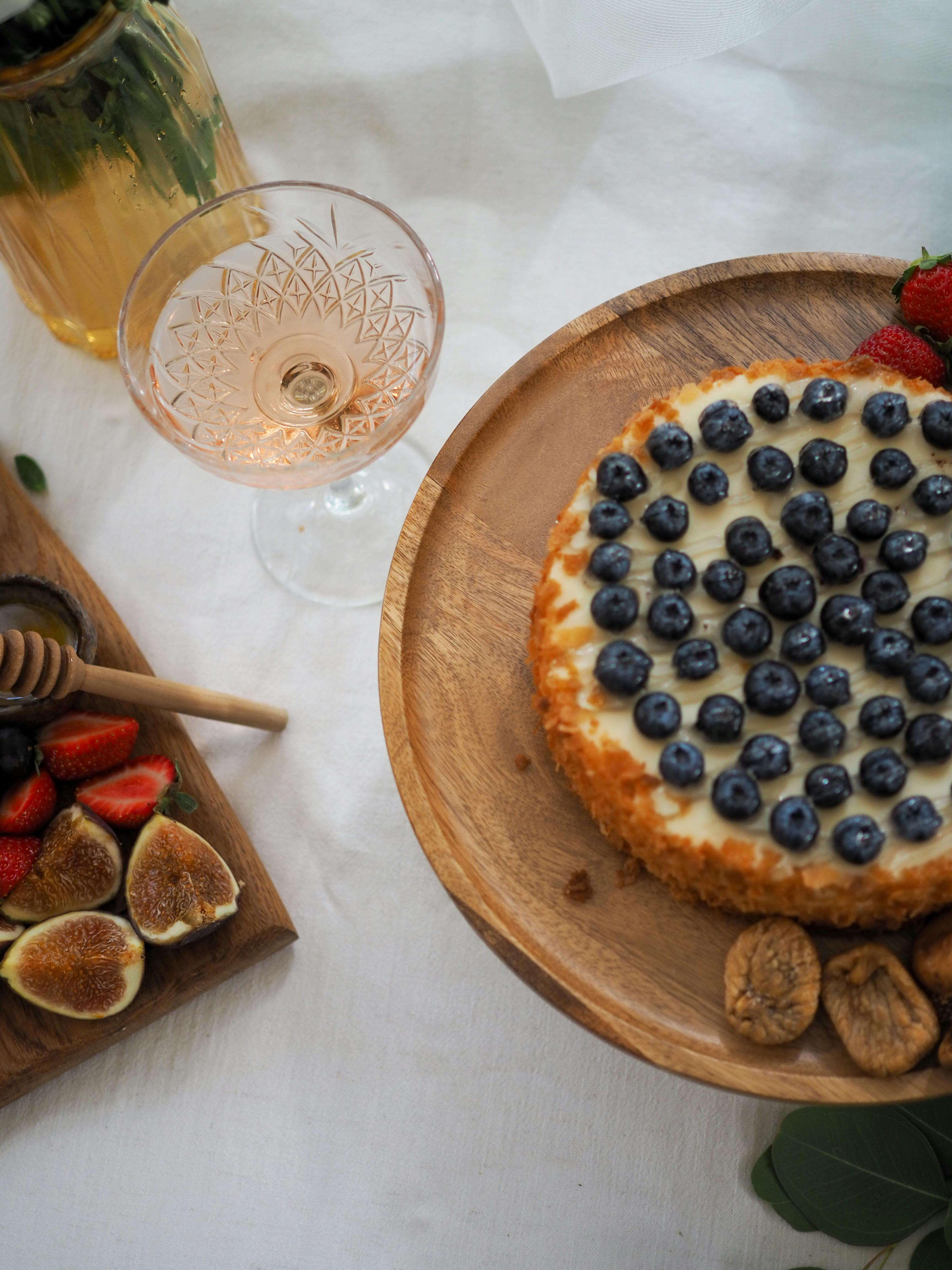 Top view of a cheesecake with blueberries, figs, and strawberries, accompanied by a glass of wine for a delightful presentation.