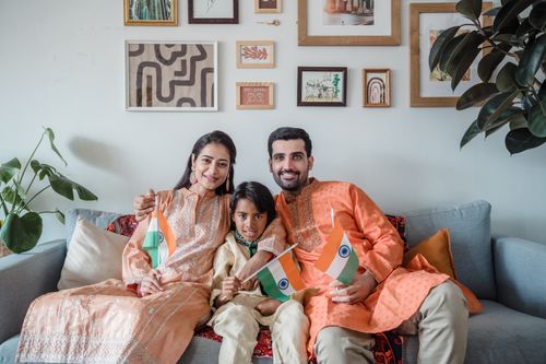 Free Indian family in traditional attire celebrating Independence Day with flags indoors. Stock Photo