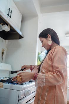 A South Asian woman in traditional clothing cooking indoors, showcasing cultural attire and cuisine.
