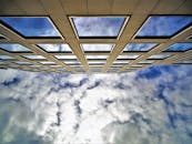 从低角度拍摄建筑立面，玻璃窗反射着多云的天空，突显出现代建筑的特色