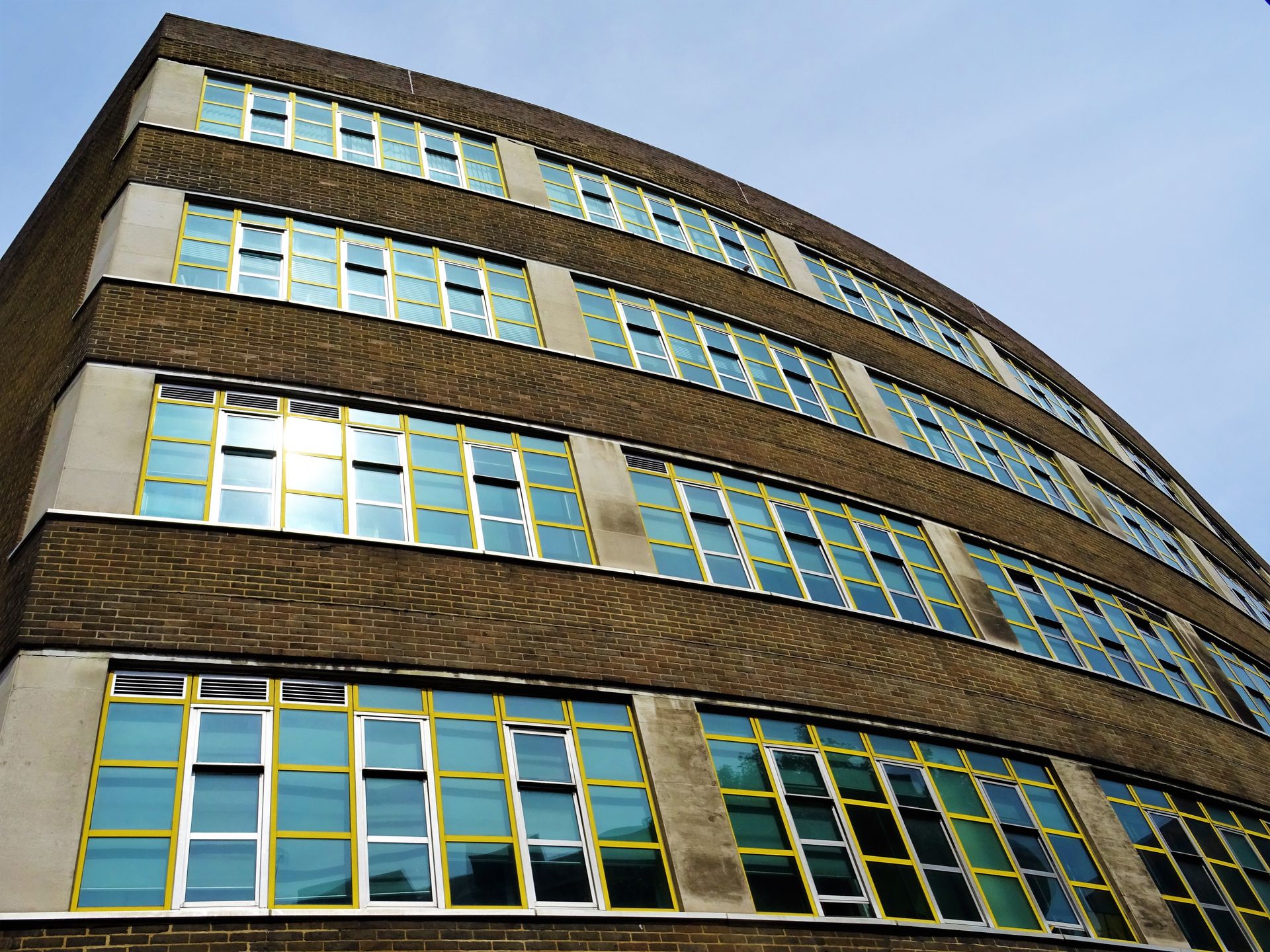 Low angle view of a modern building facade with glass windows reflecting the sky.