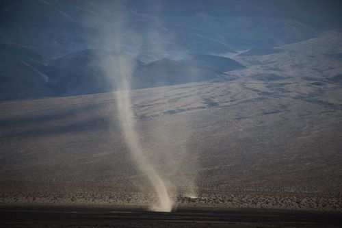 Free Aerial view of a dramatic dust devil swirling in a vast arid desert landscape under clear skies. Stock Photo