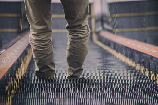 Close-up view of a person's legs standing on an escalator, capturing a modern indoor setting.