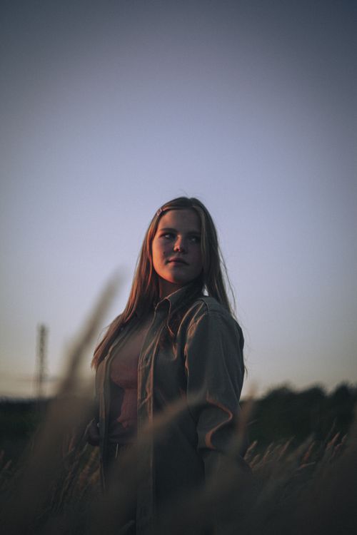 Free Portrait of a woman in a field during sunset, with long hair and serene expression. Stock Photo