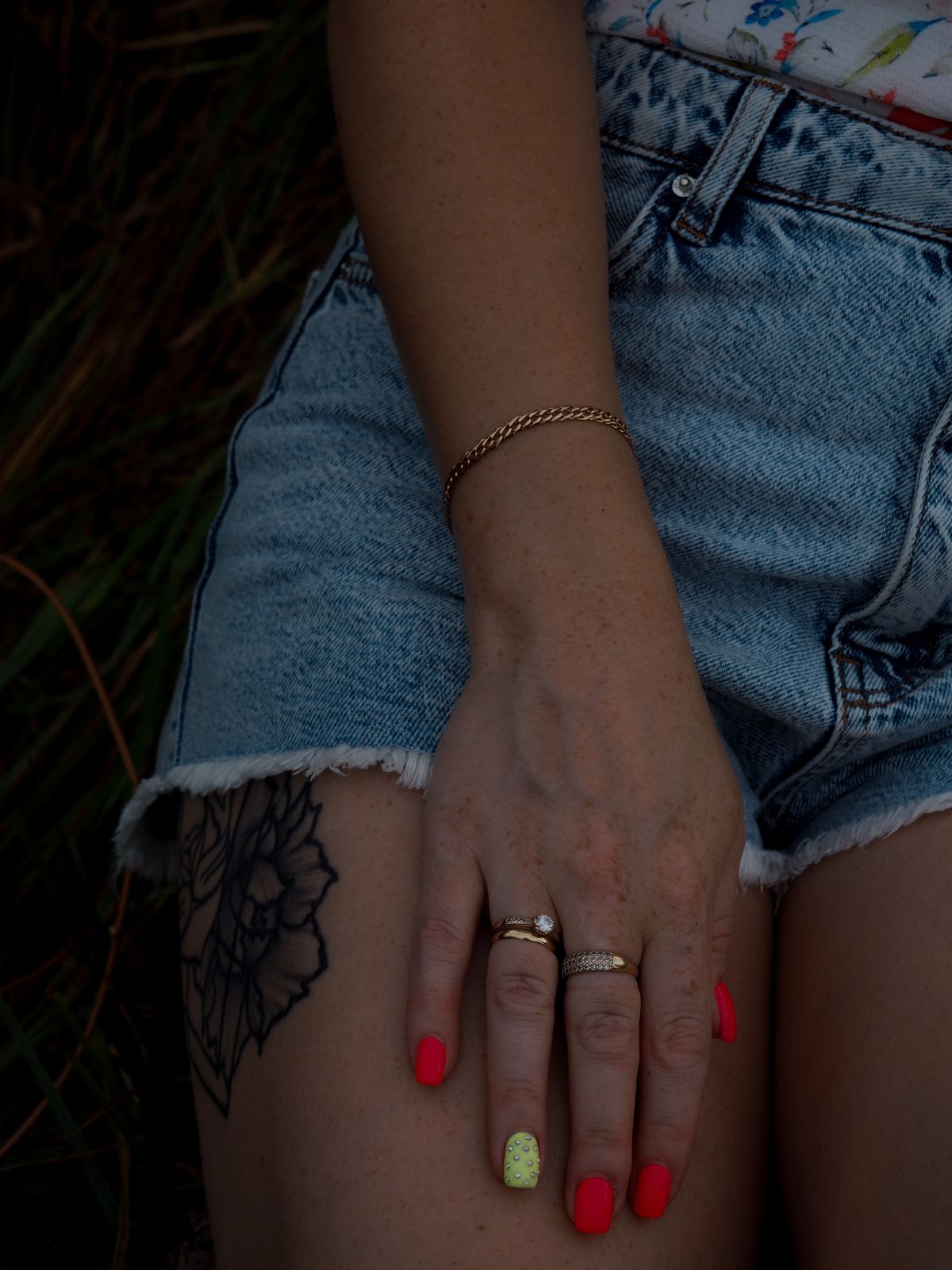 Hand with short glossy red nails and rings resting on denim shorts