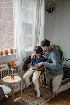 A father helps his son with a tablet indoors, surrounded by plants and natural light.