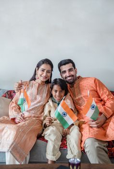 A joyful Indian family in traditional clothing holding flags inside a home setting.