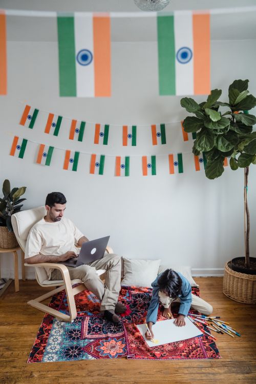 Free Father and son bonding indoors with Indian flags, using a laptop and drawing on the floor. Stock Photo