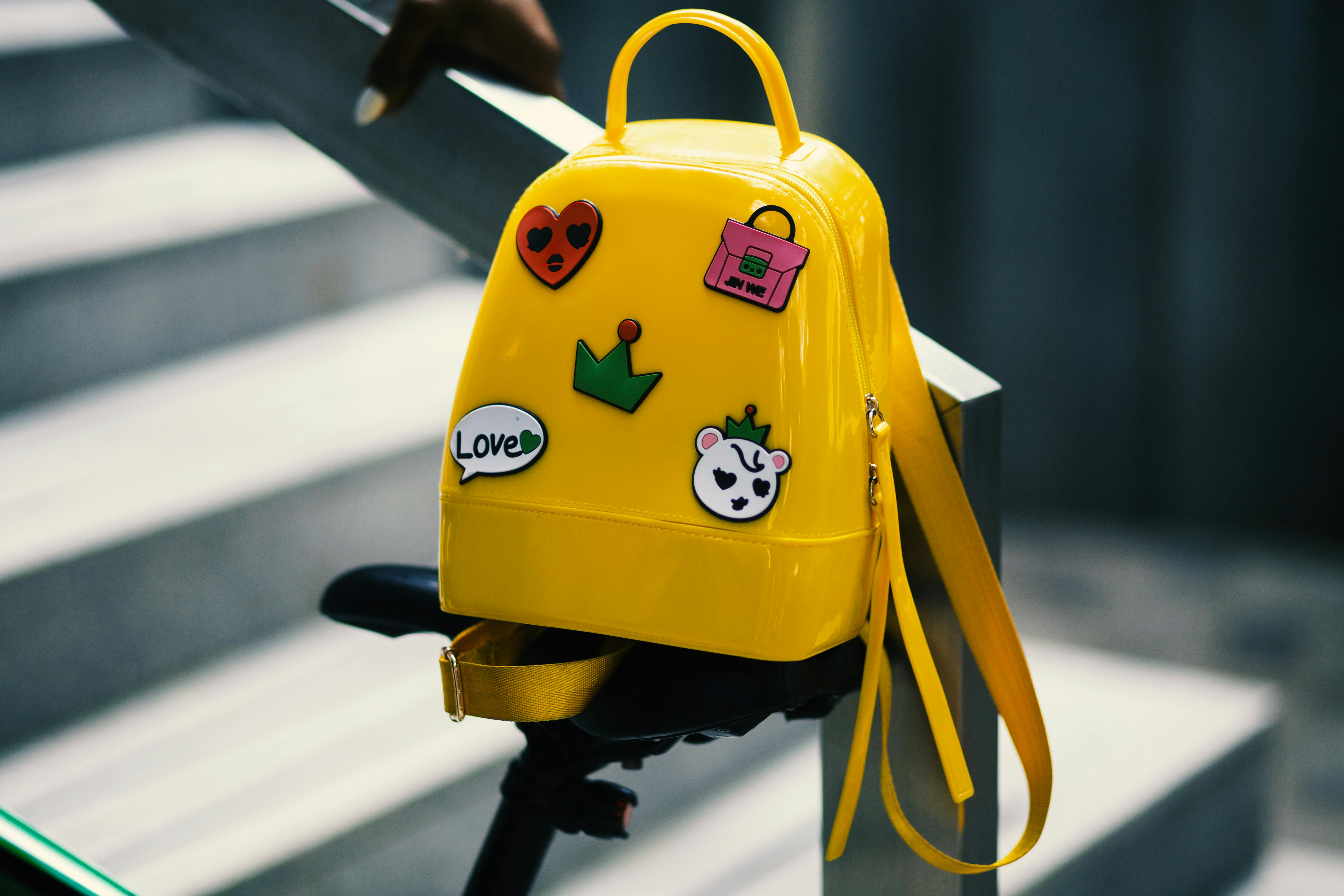 Yellow backpack with five assorted stickers on grey metal stairway rail
