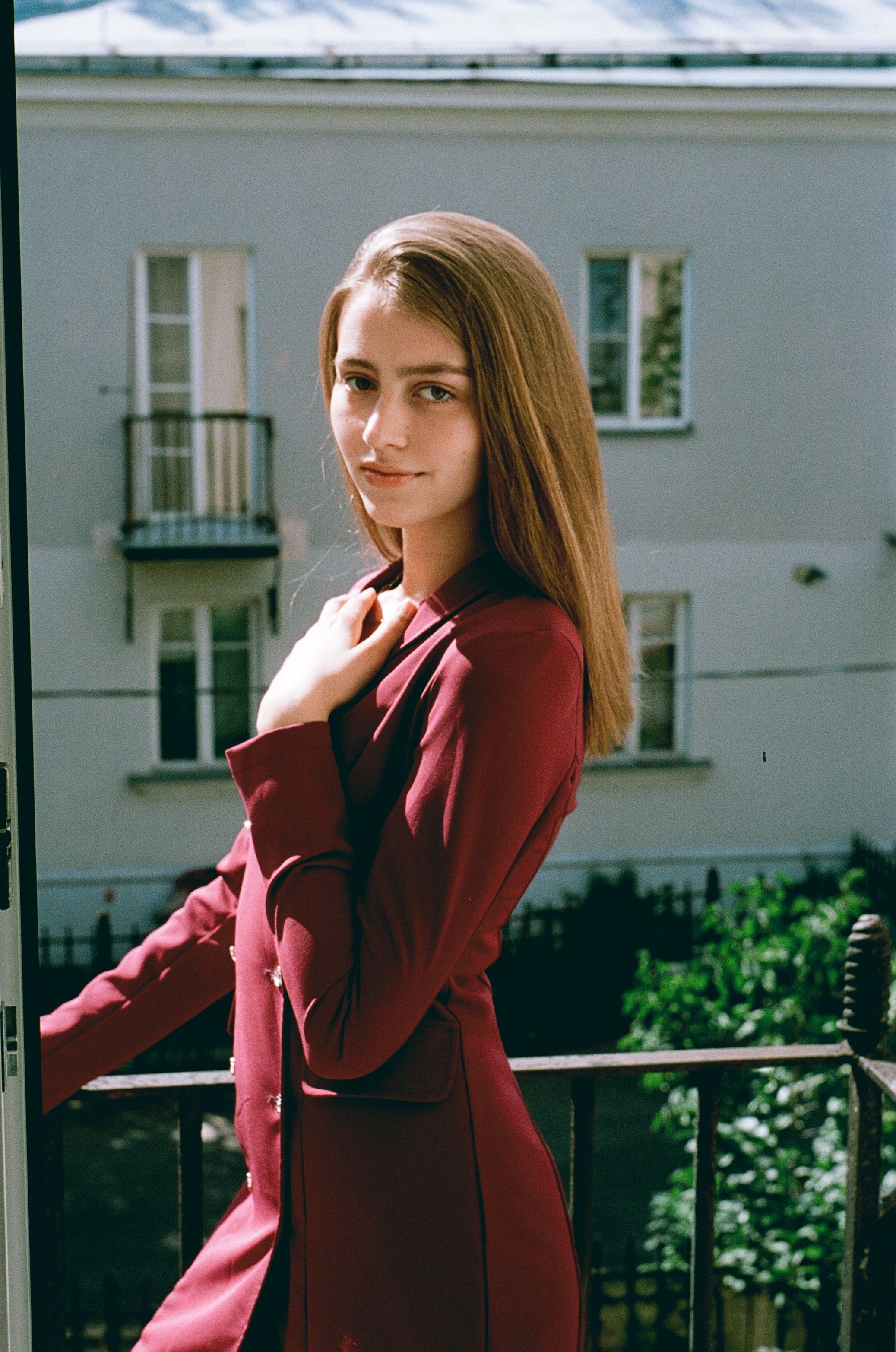 Elegant young woman in red dress posing on a balcony in St. Petersburg, Russia.