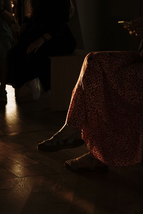 Free A serene indoor scene capturing a person in a floral dress sitting with legs crossed, illuminated by gentle sunlight. Stock Photo